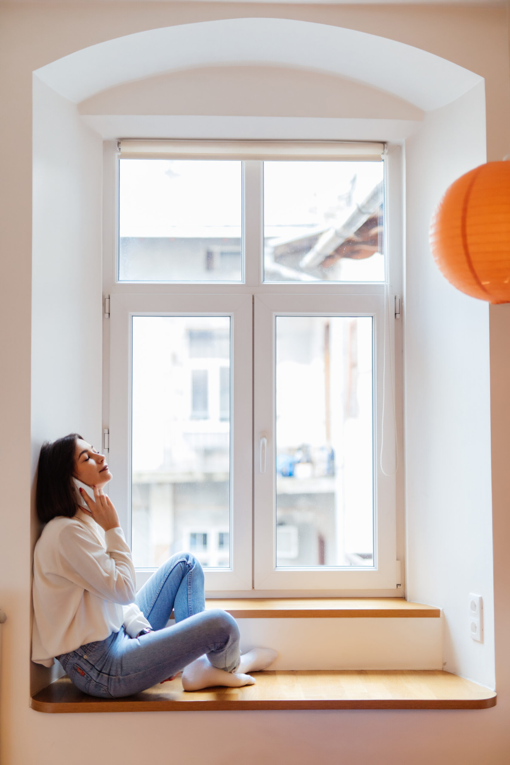 charming woman is talking on phone while sitting near the window