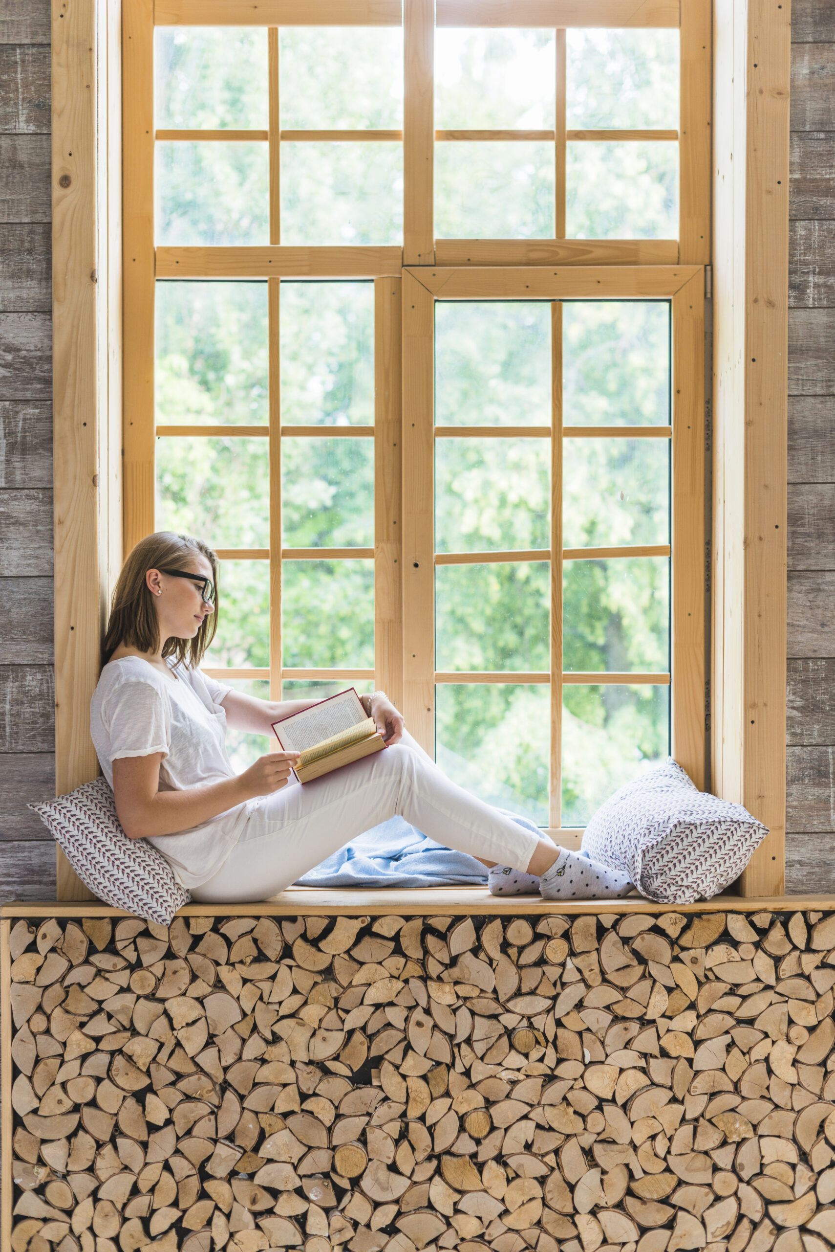 vue-laterale-de-la-jeune-femme-lisant-le-livre-assis-pres-du-rebord-de-la-fenetre